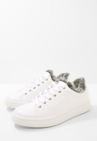Sneakers bianchi con un esterno in pelle liscia, morbido rivestimento in pelliccia sintetica grigia al colletto, punta rotonda e occhielli metallici per i lacci.