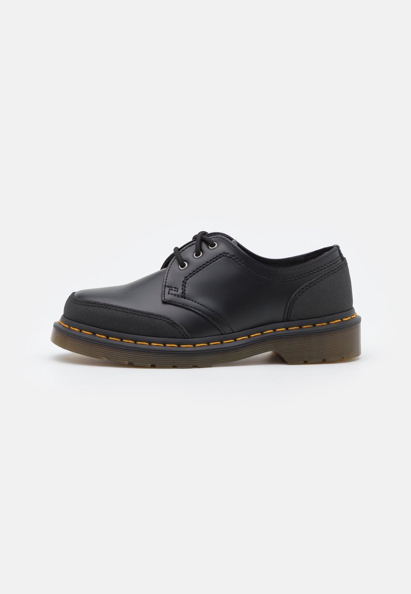Chaussures en cuir noir à lacets avec texture lisse, bout arrondi et coutures jaunes contrastantes sur la semelle. Semelle extérieure plate en caoutchouc.