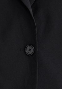 Black blazer with a textured fabric, featuring a prominent black button labeled "BOSS" and a clean, simple lapel design.