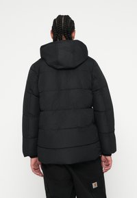 Jachetă puf vântoasă neagră cu glugă, cu un design matlasat, cusături orizontale și o textură netedă. Modelul este întors cu spatele la cameră.