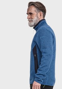 Blaue Fleecejacke mit strukturiertem Muster; seitliche Reißverschlusstasche und hoher Kragen; kontrastierende marineblaue Akzente entlang der Schultern und Tasche.