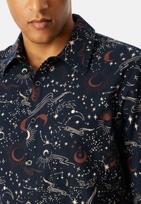 Camisa de color azul marino con un estampado temático del espacio que presenta estrellas, lunas y planetas; confeccionada con una tela de diseño texturizado y patrón, y cierre de botones.