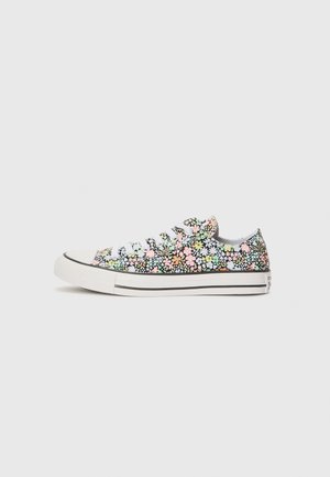 Zapatilla de lona multicolor con diseño floral, cordones blancos, puntera de goma y ribete negro. Presenta pequeñas margaritas en rosa, verde y azul.