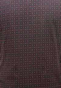 Geweven stof in donkere kleur met kleine, diamantvormige motieven in roze en rode tinten, met een gestructureerd oppervlak en ingewikkeld ontwerp.