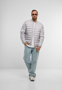 Lys grå pufferjakke med quiltet mønster, ribbet krave og lynlåslukning. Sammen med lyseblå jeans og hvide sneakers. Minimalistisk design.