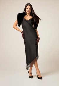 Svart satinklänning med en spetskant nedtill, kompletterad med en fuskpäls-sjal och vinröda handskar. Har tunna axelband och en figurnära siluett.