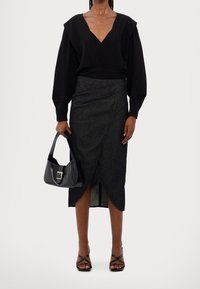 Svart långärmad topp med djup V-ringning och strukturerade axlar, kombinerad med en mörk jeanswrapkjol. Tillbehören inkluderar en svart handväska och sandaletter med remmar.