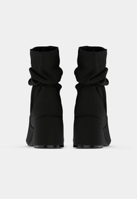 Μαύρα μποτάκια αστραγάλου με χαλαρή σχεδίαση και στρογγυλεμένη μύτη. Διαθέτουν χαμηλό τετράγωνο τακούνι και απαλό, υφασμάτινο υλικό με υφή. Μινιμαλιστικό στυλ.