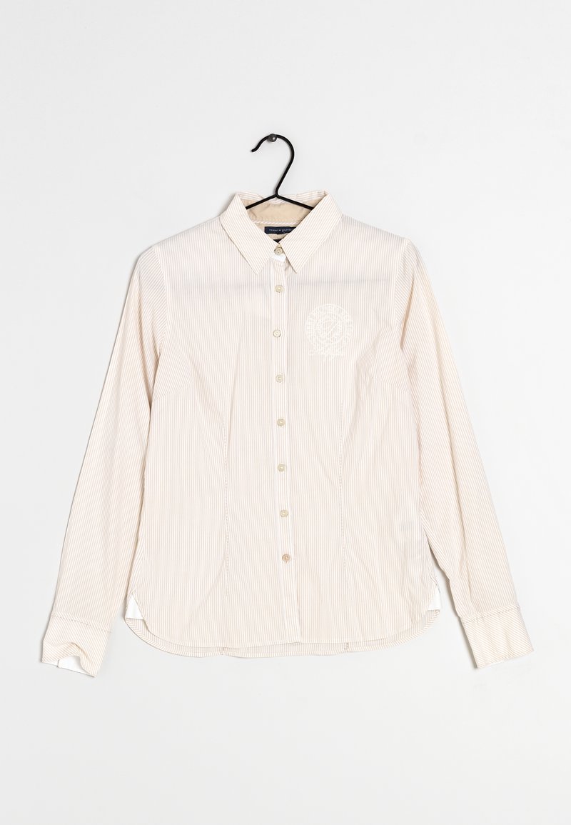 Chemise beige à manches longues avec boutons, fines rayures verticales et col, affichée sur un cintre noir sur fond blanc.