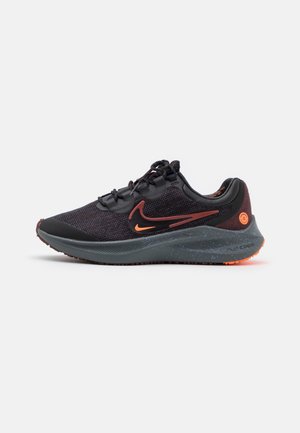 Chaussure de running Nike noire et rouge foncé avec swoosh orange, semelle intermédiaire texturée et fermeture à lacets sur fond blanc.