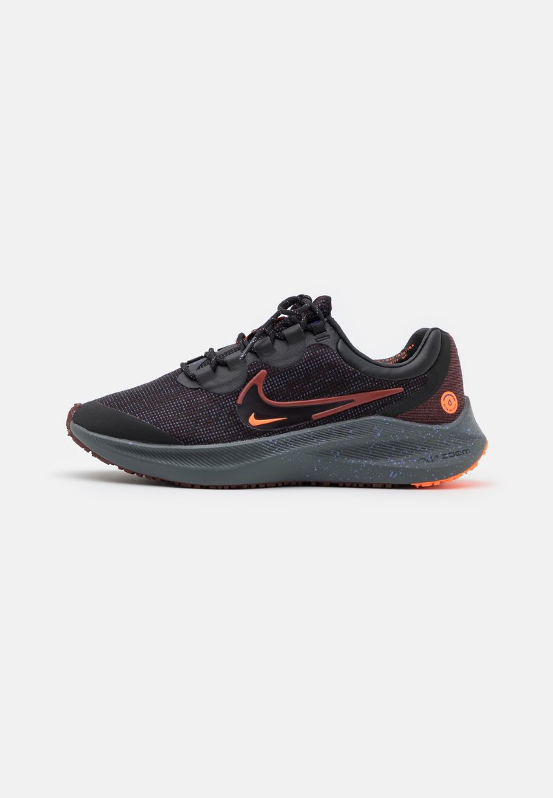 Chaussure de running Nike noire et rouge foncé avec swoosh orange, semelle intermédiaire texturée et fermeture à lacets sur fond blanc.