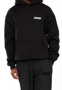 Sudadera con capucha negra hecha de mezcla de algodón, con un bolsillo frontal, capucha con cordón y logo blanco "MULTIPLY APPAREL" en el pecho izquierdo.