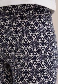 Tamsiai mėlynos leginsės su akmeninės spalvos gėlių raštu, pasižyminčiu sudėtingais dizainais ir tekstūruotu vieliniu audiniu. Įtrauktas mažas žvaigždutės akcento ženklelis.