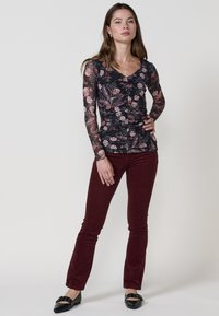 Top negro de flores con mangas largas y transparentes, diseño en capas. Combinado con pantalones acampanados de pana burdeos y zapatos planos negros.
