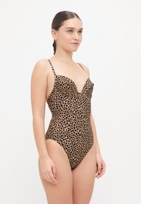 Maillot de bain une pièce à motif léopard, avec un décolleté plongeant, des bretelles fines et des ouvertures de jambe échancrées. Palette de couleurs marron et noir.