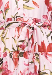 Ροζ φόρεμα με κόκκινο και πράσινο λουλουδάτο μοτίβο, με φιόγκο στη μέση και ρεβέρ λεπτομέρειες στη φάσα.