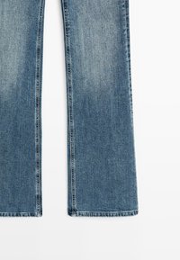 Nožky modrých džín z denimu s úzkým rovně střihem a vybledlým efektem na bílém pozadí.