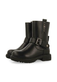 Botines de cuero negro con punta redonda, detalle de hebilla lateral y suela de goma texturizada. Presentan acentos de estrellas y una lengüeta en la parte trasera.