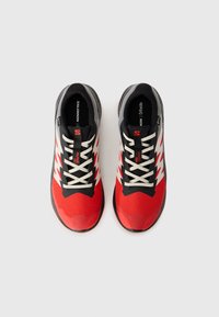 Des chaussures de sport rouges et noires avec un dessus texturé, des accents blancs et une semelle robuste. Présente un design à lacets et une structure de soutien.