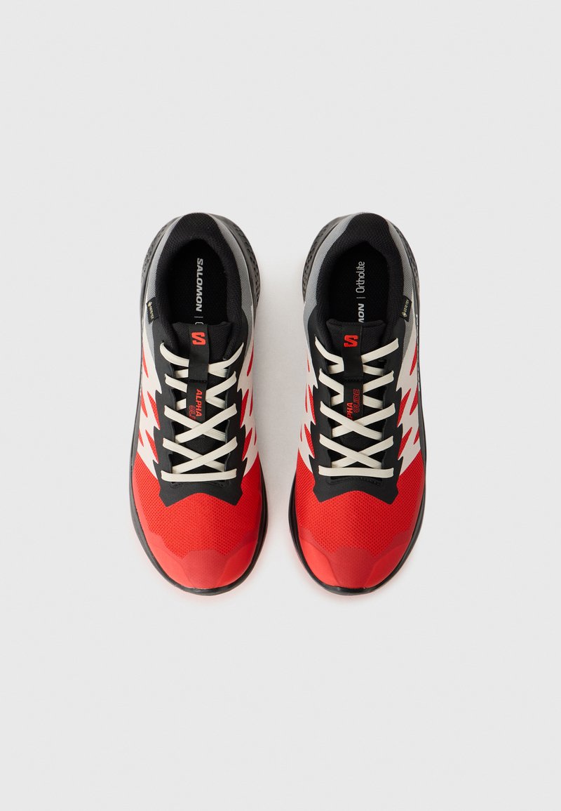Zapatillas deportivas rojas y negras con una parte superior texturizada, acentos blancos y una suela resistente. Presenta un diseño con cordones y una estructura de soporte.