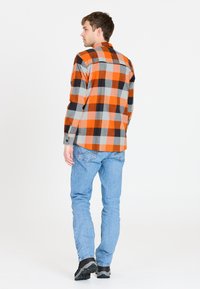 Ternede flannel skjorte i orange og grå nuancer, med lange ærmer og knapmanchetter, bæret over blå jeans og sort fodtøj.