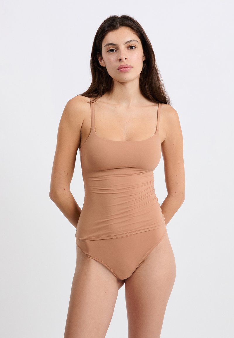 Costume da bagno a pezzo unico marrone, aderente, con spalline sottili, tessuto liscio e dettagli arricciati sui lati. Apertura della gamba alta in stile classico.