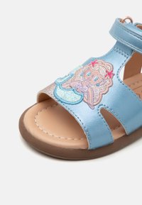 Blå faux skinn sandal med åpen tå-design. Har et skinnende sølvdetalj og fargerik brodert karakterdetalj. Gummisåle.