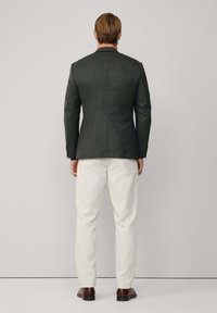 Tmavosivý priliehavý blejzer so štruktúrovaným strihom, skombinovaný s bielymi nohavicami. Disponuje hladkou textúrou a klasickým dizajnom goliera.