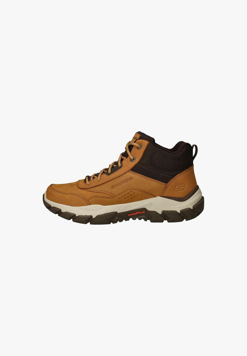Baskets Skechers montantes mi-hautes marron et noir avec semelle blanche et bande de roulement Goodyear, lacets à l'avant et languette au talon.