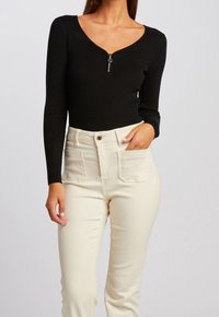 Body noir côtelé à manches longues avec un col en V et une fermeture éclair, associé à un pantalon crème taille haute avec deux poches avant.