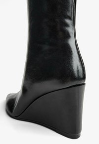 Fekete, csillogó bőr ankle boot sarok, hegyes orral és ívelt, emelt sarkú kialakítással a nagyobb magasság és a kényelem érdekében.