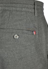 Grijze stofbroek met subtiele textuur, voorzien van een plastic knoopsluiting en geborduurd logo. Accent gestreepte details bij de zak.
