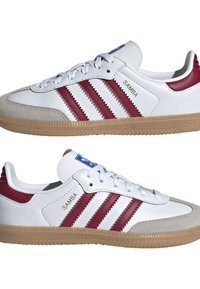 Baskets en cuir blanc avec des accents rouges, présentant trois bandes rouges, une semelle en gomme et un capuchon en daim. Nom de la marque "Samba" en doré.