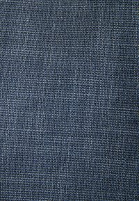 Gros plan d’un tissu tissé serré bleu foncé et gris avec un motif texturé en forme de grille.