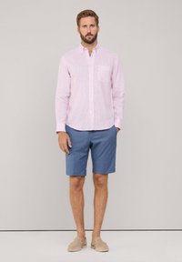 Lichtroze gestreepte button-up shirt met een zak, gecombineerd met blauwe shorts en beige instap schoenen. Casual zomeroutfit.