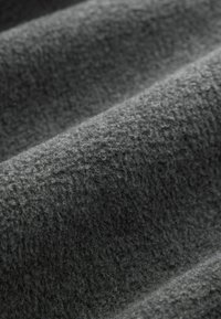 Tessuto grigio scuro con una superficie morbida e pelosa, che mostra un aspetto ondulato e stratificato. Ideale per abbigliamento o arredamenti morbidi.