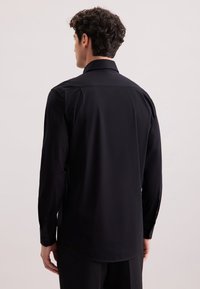 Maglietta nera a maniche lunghe con una texture liscia, polsini con bottoni, colletto classico e orlo dritto. Adatta per ambienti formali.