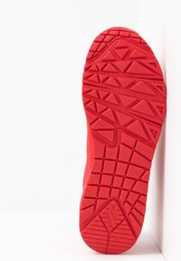 Röd sportskosula med texturerad gummi, med ett zigzag- och triangelmönster för grepp, lutad mot en vit bakgrund.