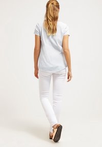 Světle modrá košile s krátkým rukávem a zakulaceným lemem, doplněná o úzce střižené bílé džíny a hnědé sandály se strukturovanou podrážkou.