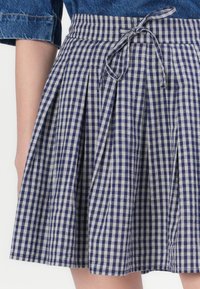 Jūras kara flotes un baltā gingham plisētā svārku ar jostu, kurai ir teksturēta auduma un vertikālas plisītes, izceļot ikdienišķu dizainu.