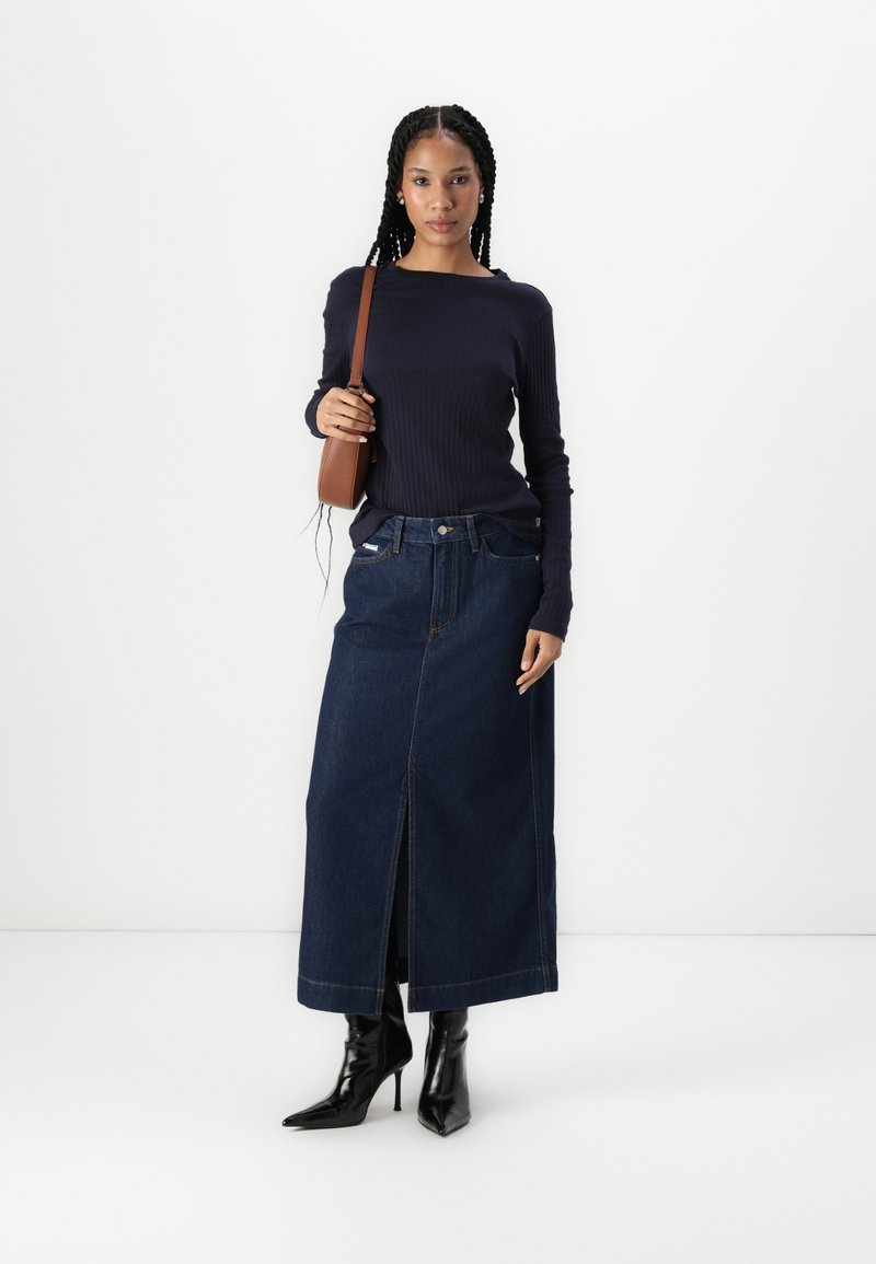 Marineblaues, geripptes Langarmoberteil, kombiniert mit einem Maxirock aus dunkelblauem Denim, der einen Frontschlitz hat, sowie schwarzen spitzen Ankle Boots. Dazu eine braune Umhängetasche.