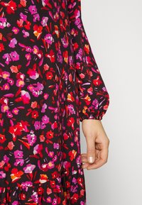 Sukienka w kwiatowy wzór na czarnym tle, z różowymi, czerwonymi i pomarańczowymi kwiatami. Długie, bufiaste rękawy z elastycznymi mankietami i falbaną na dole.