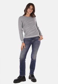 Maglione grigio a maglia con un motivo testurizzato, scollatura rotonda e orlo a coste, abbinato a jeans di denim blu e stivali neri con lacci.