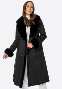 Abrigo negro con un collar y puños de piel sintética, diseño de doble botonadura, textura suave y lazos laterales para ajuste, presentando una silueta elegante.