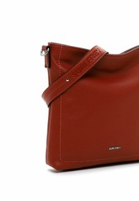 Red leather handbag with a smooth texture, featuring a silver-tone ring, adjustable strap, and embossed brand name. Rectangular shape.