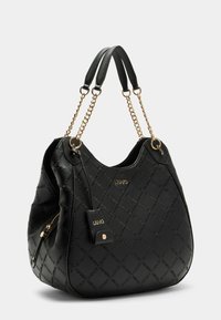 Sac à épaule en cuir noir avec texture matelassée, accents en chaîne dorée et tag logo suspendu. Il possède une poche zippée pour la fermeture.