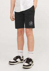 Zwarte katoenen shorts met een geribde tailleband, zijzakken en een wit logodetail. Gecombineerd met zwart-witte sneakers en witte crew-sokken.