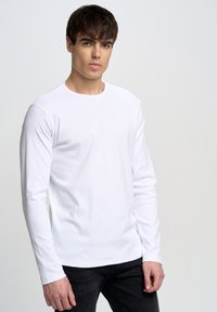 Langærmet hvid bomulds T-shirt med en enkel rund halsudskæring. Glat tekstur, tætsiddende design med lige ærmer og klassisk snit.