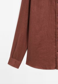 Brown linen shirt with a button-up front, long sleeves, and a classic collar. The fabric has a textured finish and a curved hemline.