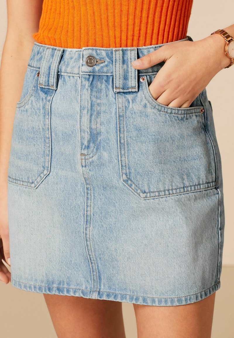 Gonna di jeans azzurro chiaro con vita alta, dotata di tasche frontali, chiusura con bottone e taglio dritto, abbinata a un top arancione a coste.